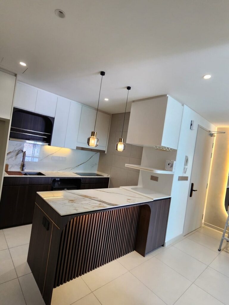 A modern open kitchen with marble-look waterfall island, dark wood and white cabinetry. Alix Residences, Petaling Jaya, Selangor.