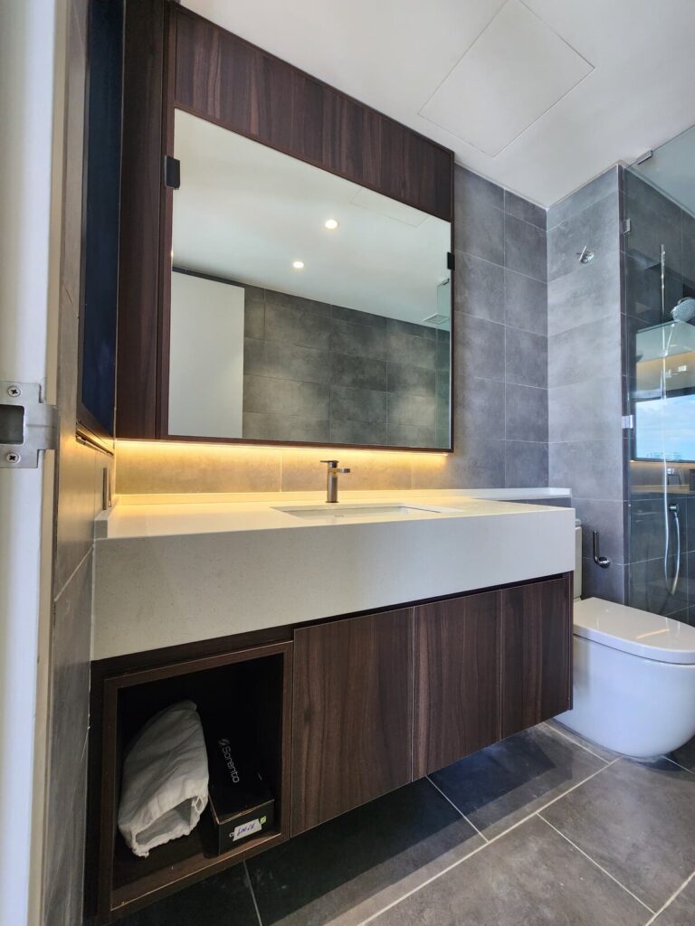 Bathroom with a dark wood-framed mirror, white quartz countertop with undermount sink, dark wood vanity and a wall-hung toilet. Alix Residences, Petaling Jaya, Selangor.