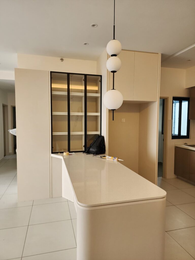 Completed open-plan kitchen with a cream curved peninsula counter, three-globe pendant light and black-framed glass display cabinet. Alix Residences, Petaling Jaya, Selangor.