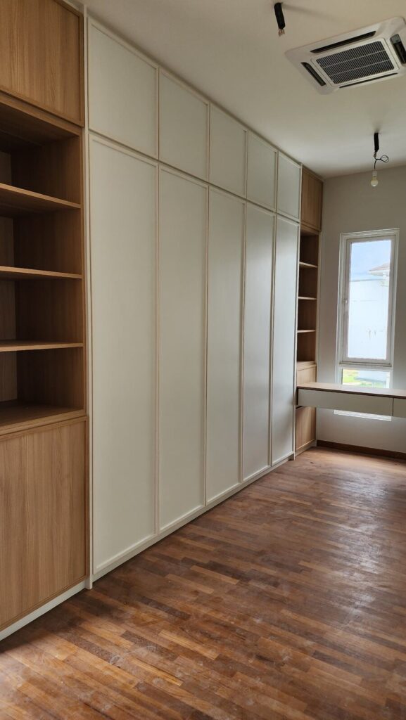 Room with wooden floor, extensive built-in storage combining white panelled wardrobes and open wood shelving. Jade Hills, Kajang, Selangor.