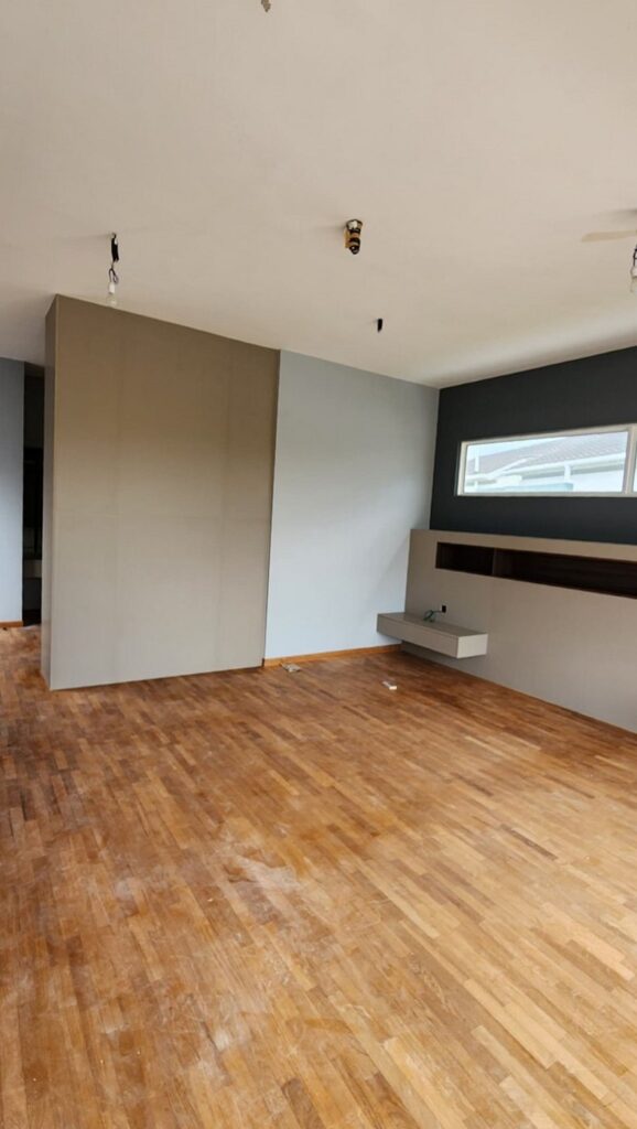 Room with wooden parquet floor, partial dividing wall, grey accent wall with a long window, and a floating shelf and ledge. Jade Hills, Kajang, Selangor.