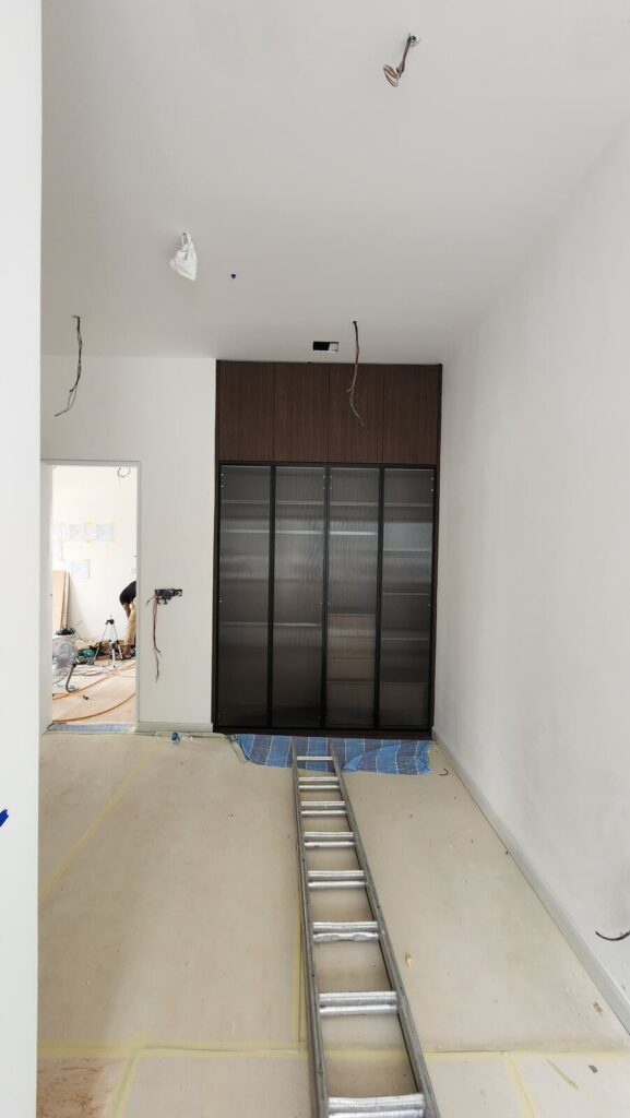Installed full-height built-in cabinet with dark wood upper doors and ribbed/fluted glass lower doors against a white wall. Jardin Residence, Kuala Lumpur.