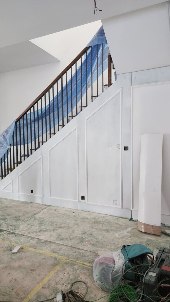 Staircase with black metal balusters and wooden handrail over white panelled under-stair wall. Jardin Residence, Kuala Lumpur.