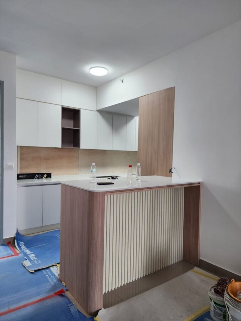 Open-plan kitchen with white upper cabinets, open shelving niche, plywood backsplash and a wood-veneer peninsula with slatted side panel. M Zenya, Kuala Lumpur.