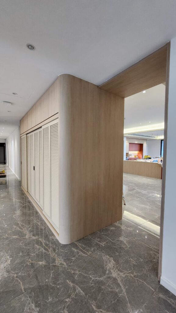 Finished corridor with polished marble floor, a curved wood-veneer partition with louvered cabinet doors. Park Regent, Desa ParkCity, Kuala Lumpur.