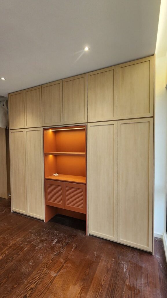 Finished built-in floor-to-ceiling wardrobe cabinetry in light wood with an orange open shelving/desk niche. Park Regent, Desa ParkCity, Kuala Lumpur.