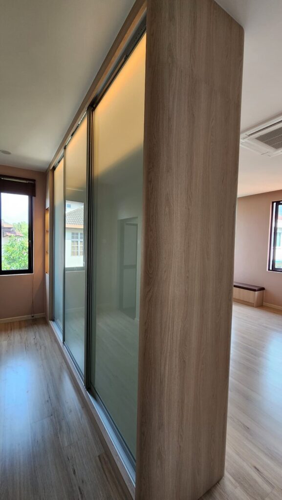 Walk-in space with a tall frosted-glass sliding-door wardrobe and a curved wood-grain partition column. Saujana Akasia, Shah Alam, Selangor.